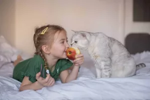Pisica și fetița care mănâncă un măr; sursă foto: AZ Animals.com